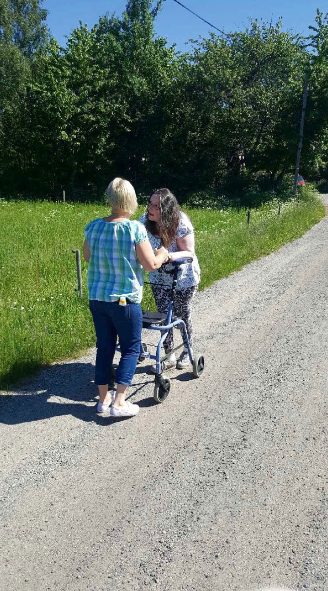 To kvinner går sammen langs en sti, den ene med rullator